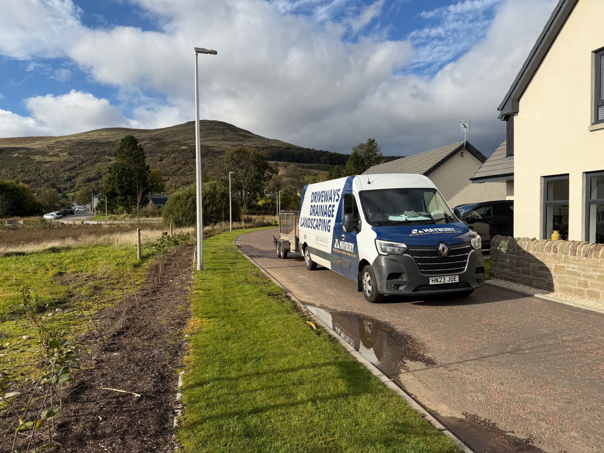 Maybury Landscaping van beside a stone-walled home, with green verges, Scottish hills and a blue, cloud-filled sky